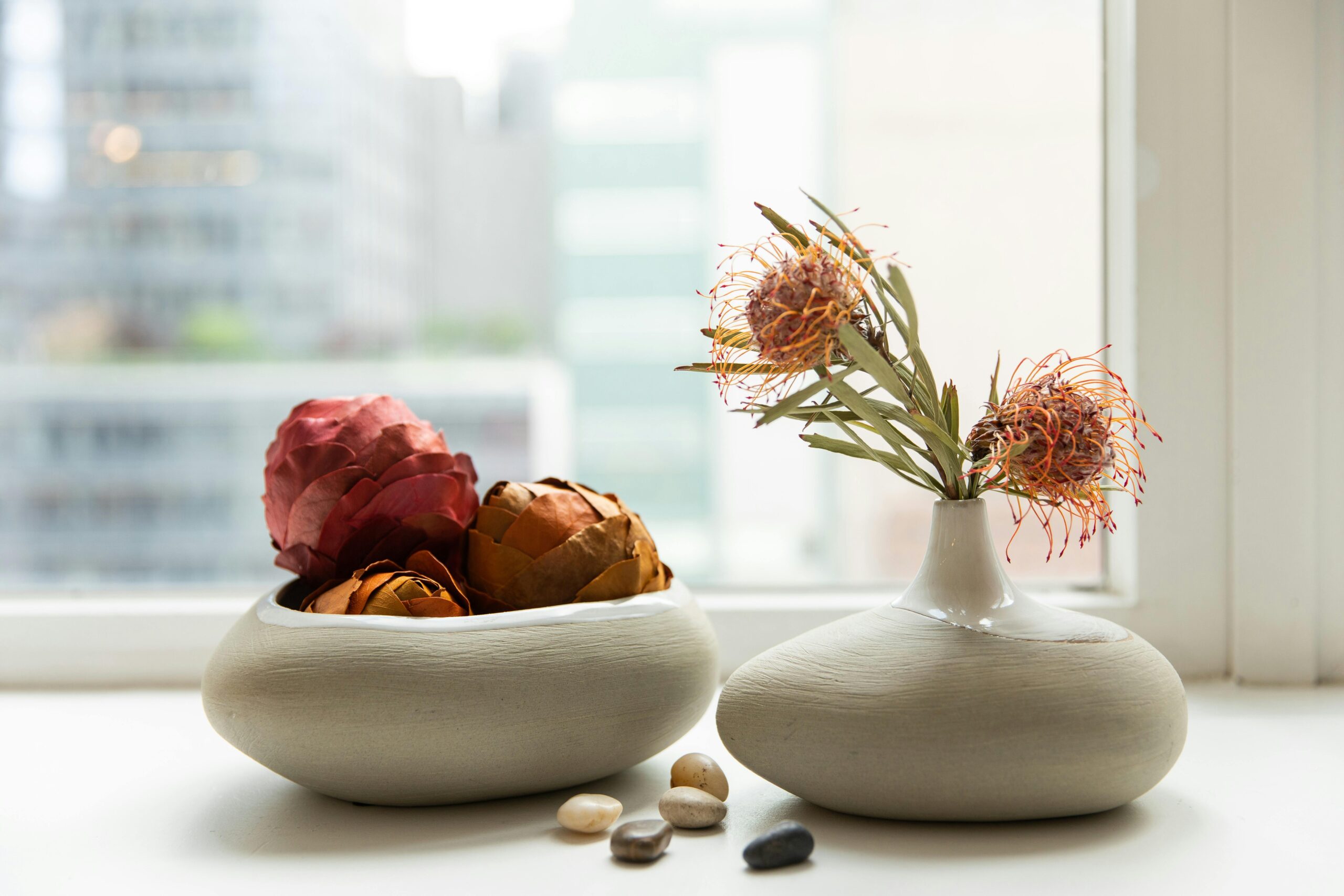 Stylish flower vases with dried protea flowers and stones on a modern window sill.