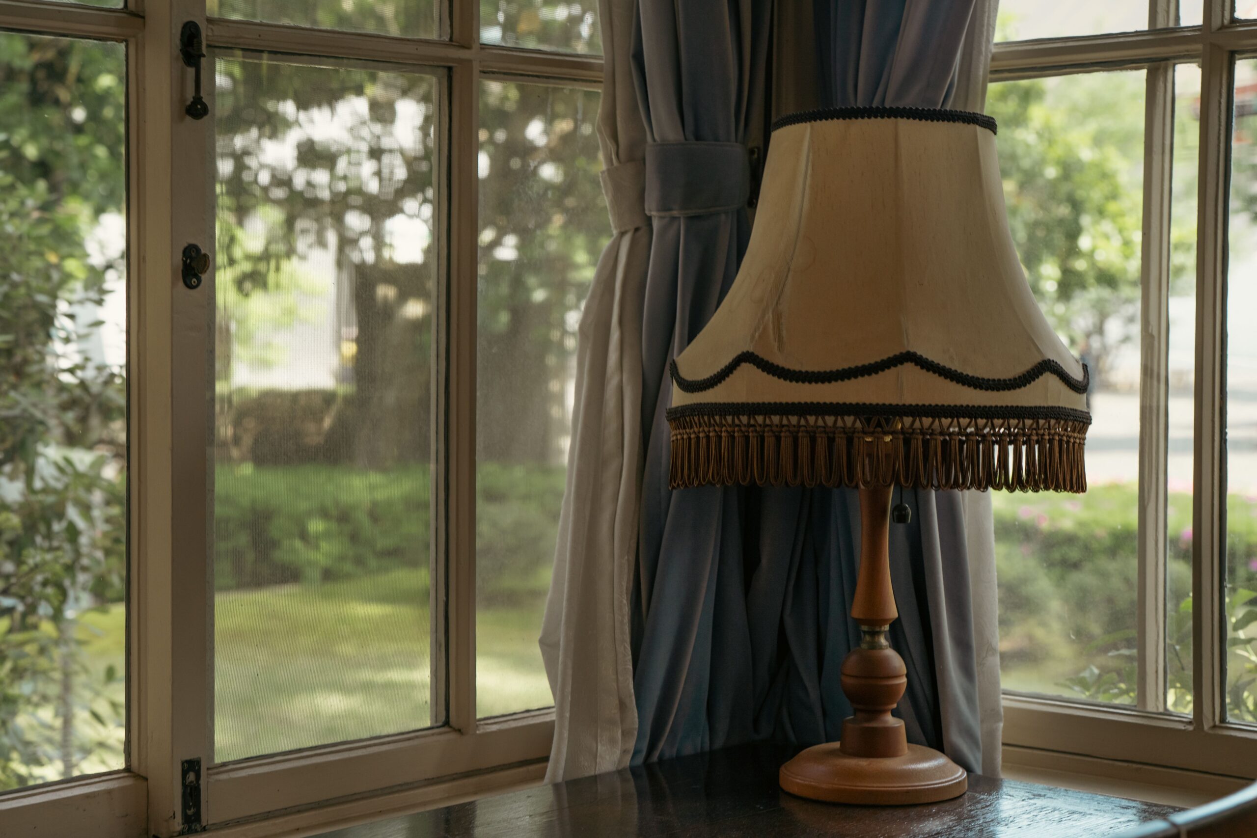 Cozy interior with a vintage lamp and curtains by a window overlooking a lush garden.